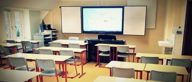 Unterrichtsraum in einer Schule mit leeren Schulbänken, digitaler Tafel und einem Klavier - zur Artikelseite Fragen zu Schulen und Tageseinrichtungen für Kinder