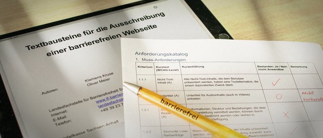 Tablet mit geöffneter Datei Leitfaden für die Ausschreibung barrierefreier Webseiten. Daneben liegt der Anforderungskatalog Barrierefreiheit auf Papier gedruckt und ein Kugelschreiber mit der Aufschrift barrierefrei