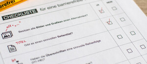 eine ausgedruckte Checkliste und ein Kugelschreiber mit der Aufschrift Barrierefreiheit liegen auf einem Schreibtisch