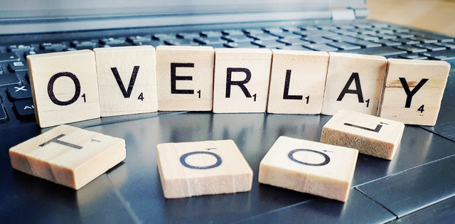 Kleine Holzblöcke mit Buchstaben beschriftet bilden das Wort Overlay und liegen auf einer Laptop-Tastatur