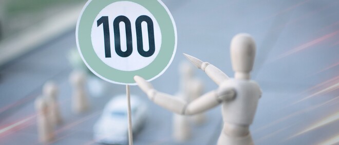 Verkehrsschild mit Zahl 100 und Holzfigur zeigt darauf - zur Artikelseite &Uuml;berwachungsstellenbericht 2025