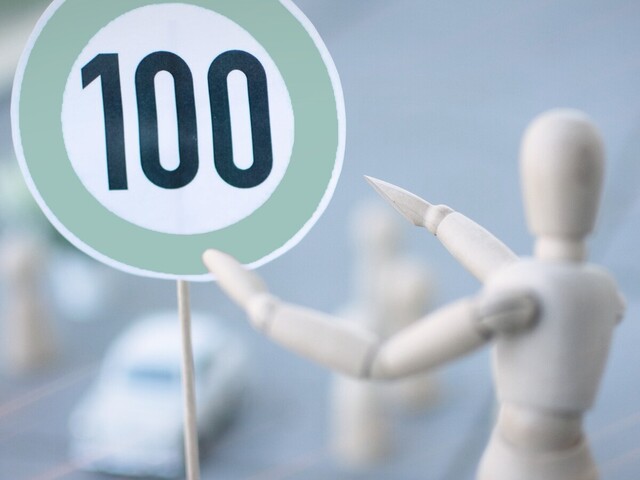 Verkehrsschild mit Zahl 100 und Holzfigur zeigt darauf - zur Artikelseite &Uuml;berwachungsstellenbericht 2025