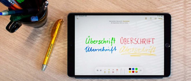 Tablet, Kugelschreiber und Tasse auf einem Schreibtisch. Tablet zeigt 4 Mal das Wort Überschrift in unterschiedlichen Farben und Schriftarten - zur Artikelseite Überschriften.