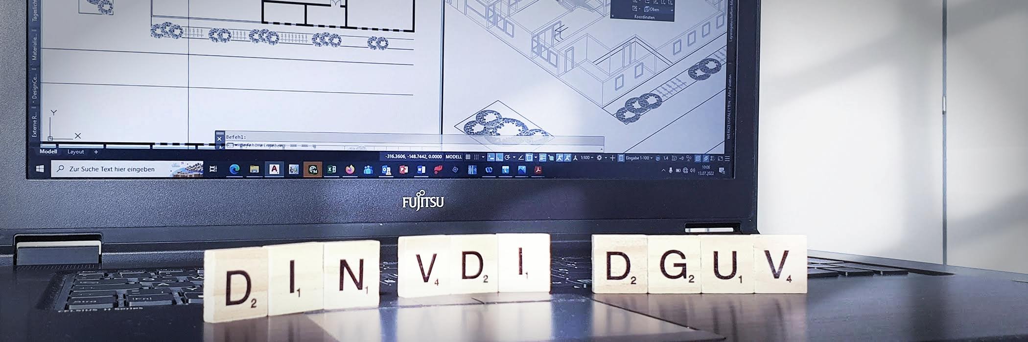 vor einem Laptopbildschirm stehen Holzbuchstaben mit den Abkürzungen DIN, VDI und DGUV 