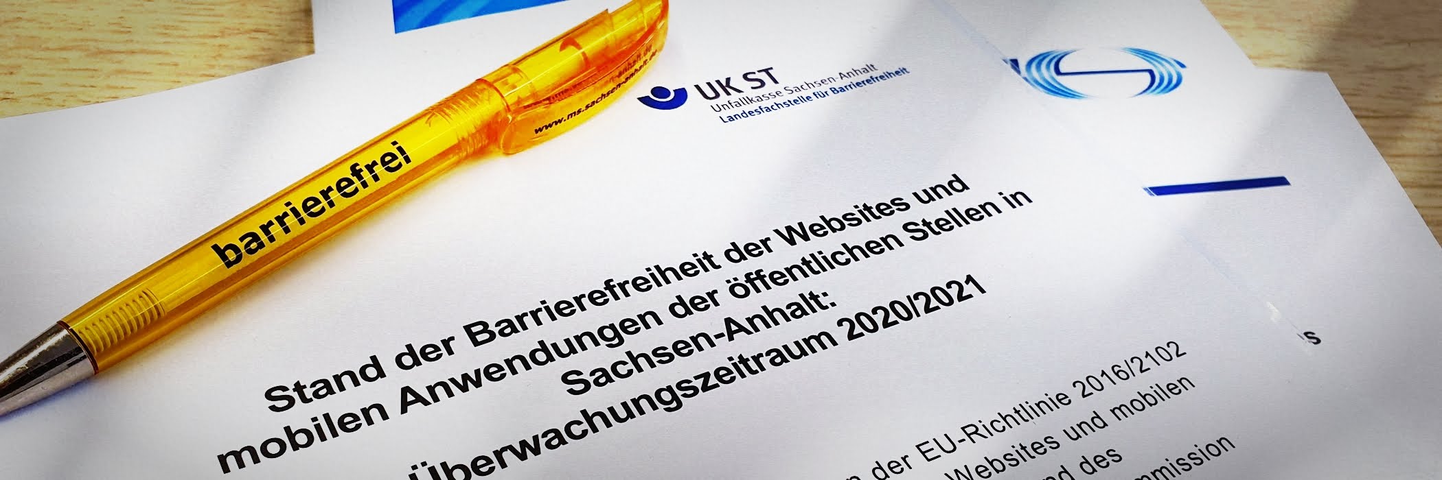 Deckblatt des Berichts mit dem Titel "Stand der Barrierefreiheit der Websites und mobilen Anwendungen der öffentlichen Stellen in Sachsen-Anhalt: Überwachungszeitraum 2020/2021“. Darauf liegt ein gelber Kugelschreiber mit dem Wort „barrierefrei".