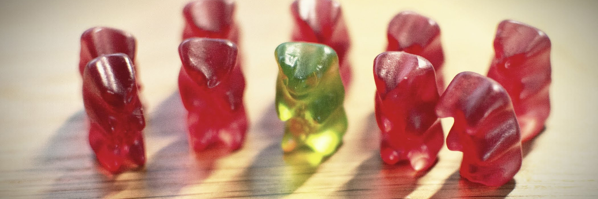 9 rote Gummibärchen und ein grüner stehen in 2 Reihen auf einem Tisch