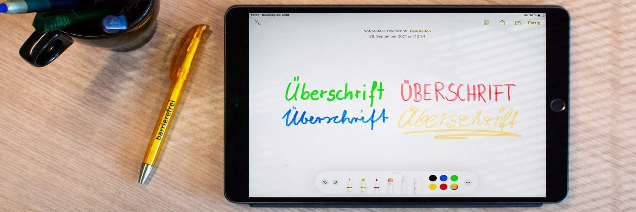 Tablet, Kugelschreiber und Tasse auf einem Schreibtisch. Tablet zeigt 4 Mal das Wort Überschrift in unterschiedlichen Farben und Schriftarten