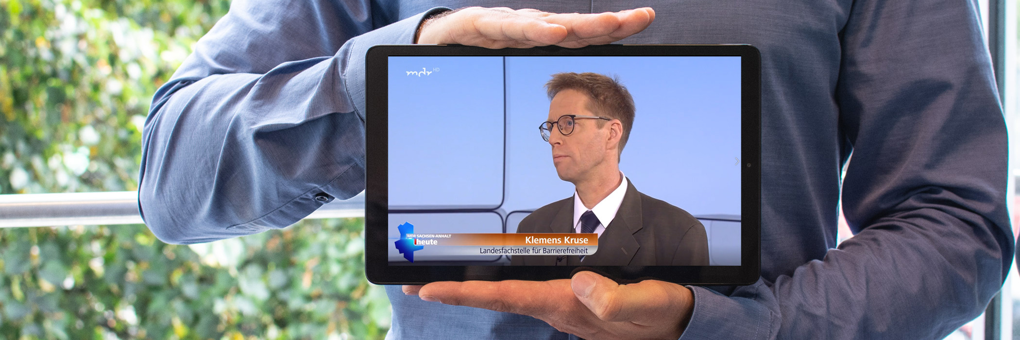 Eine Person hält ein Tablet in der Hand. Auf diesem ist der Leiter der Landesfachstelle Sachsen-Anhalt, Herr Kruse, bei einem Interview zu sehen.