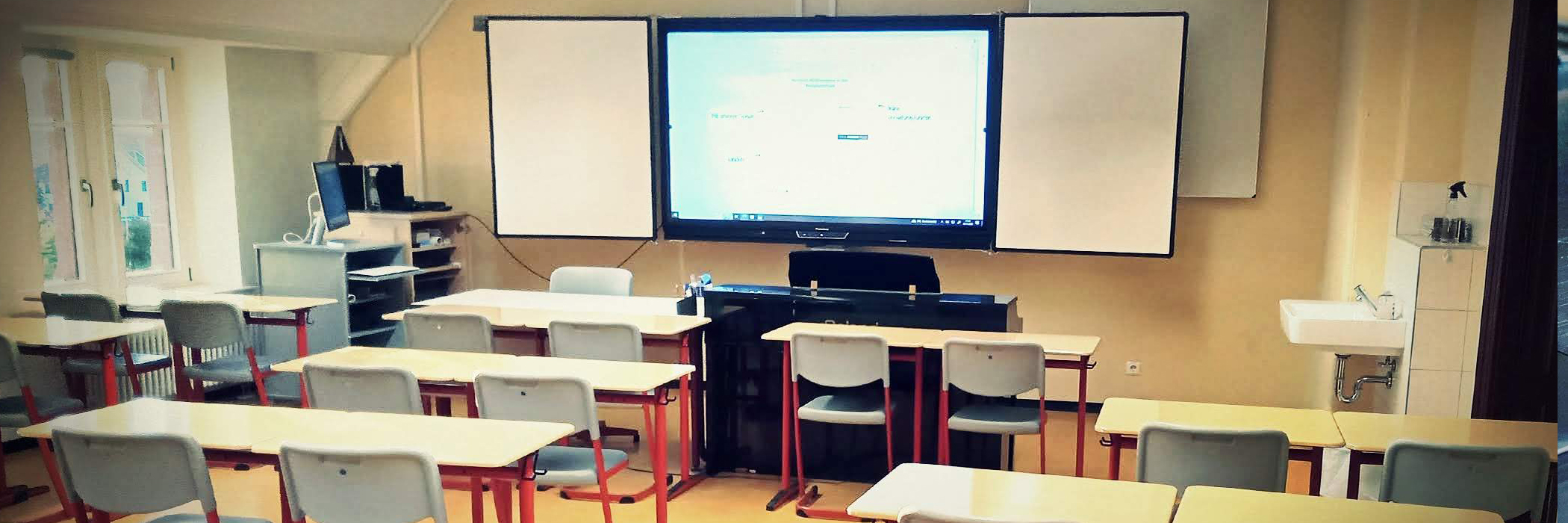 Unterrichtsraum in einer Schule mit leeren Schulbänken, digitaler Tafel und einem Klavier