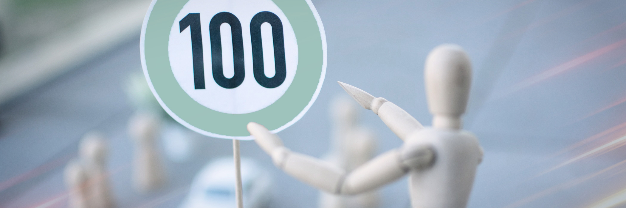 Verkehrsschild mit Zahl 100 und Holzfigur zeigt darauf