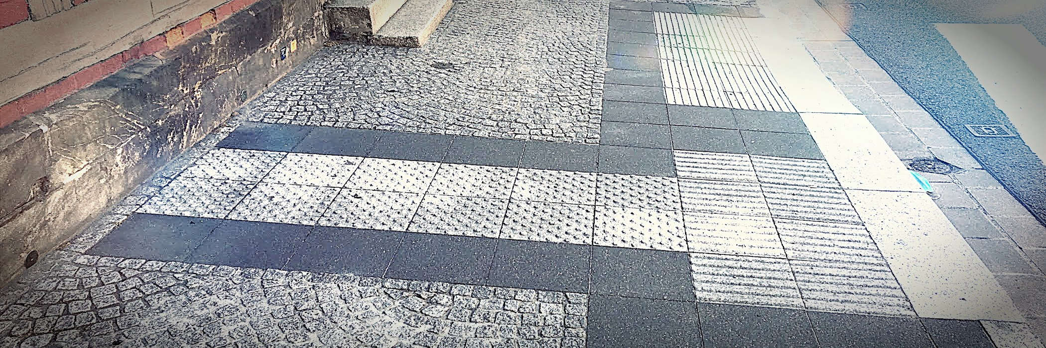 Teil eines Blindenleitsystems auf einem Fußweg: Das Blindenleitsystem zeigt an, wo Menschen die Straße sicher überqueren können