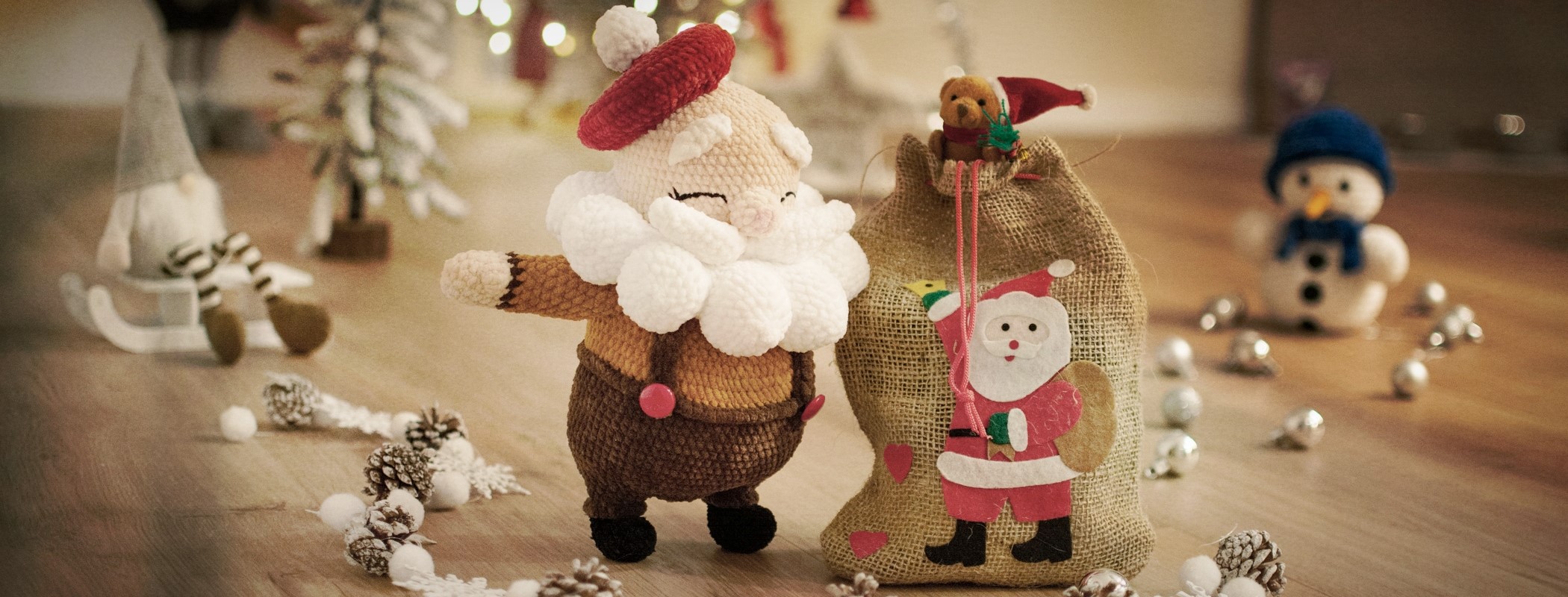 Ein geh&auml;kelter Weihnachtsmann steht in einer Weihnachtslandschaft neben seinem Rucksack mit den Geschenken. Er blickt freundlich und wirkt sehr zufrieden.