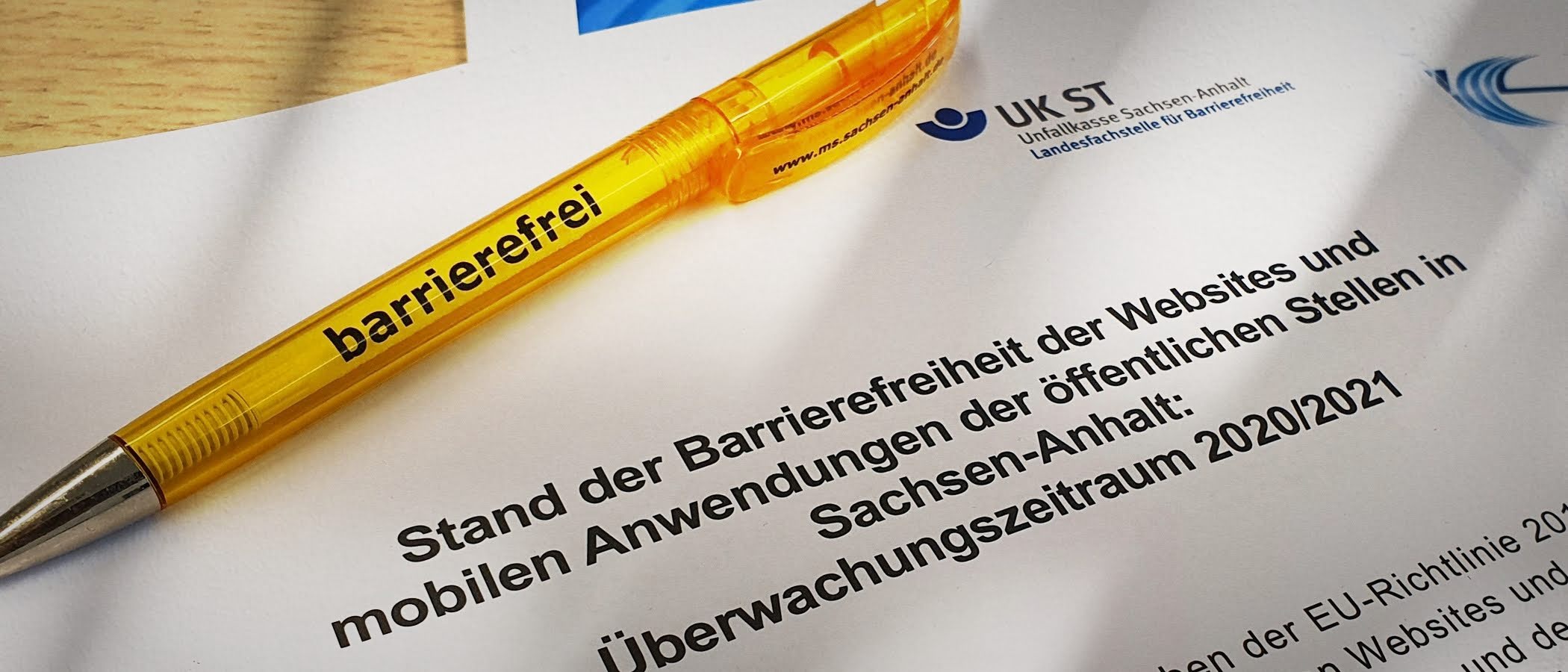 Deckblatt des Berichts mit dem Titel „Stand der Barrierefreiheit der Websites und mobilen Anwendungen der öffentlichen Stellen in Sachsen-Anhalt: Überwachungszeitraum 2020/2021“. Darauf liegt ein gelber Kugelschreiber mit dem Wort „barrierefrei - zur Artikelseite Bericht 2021