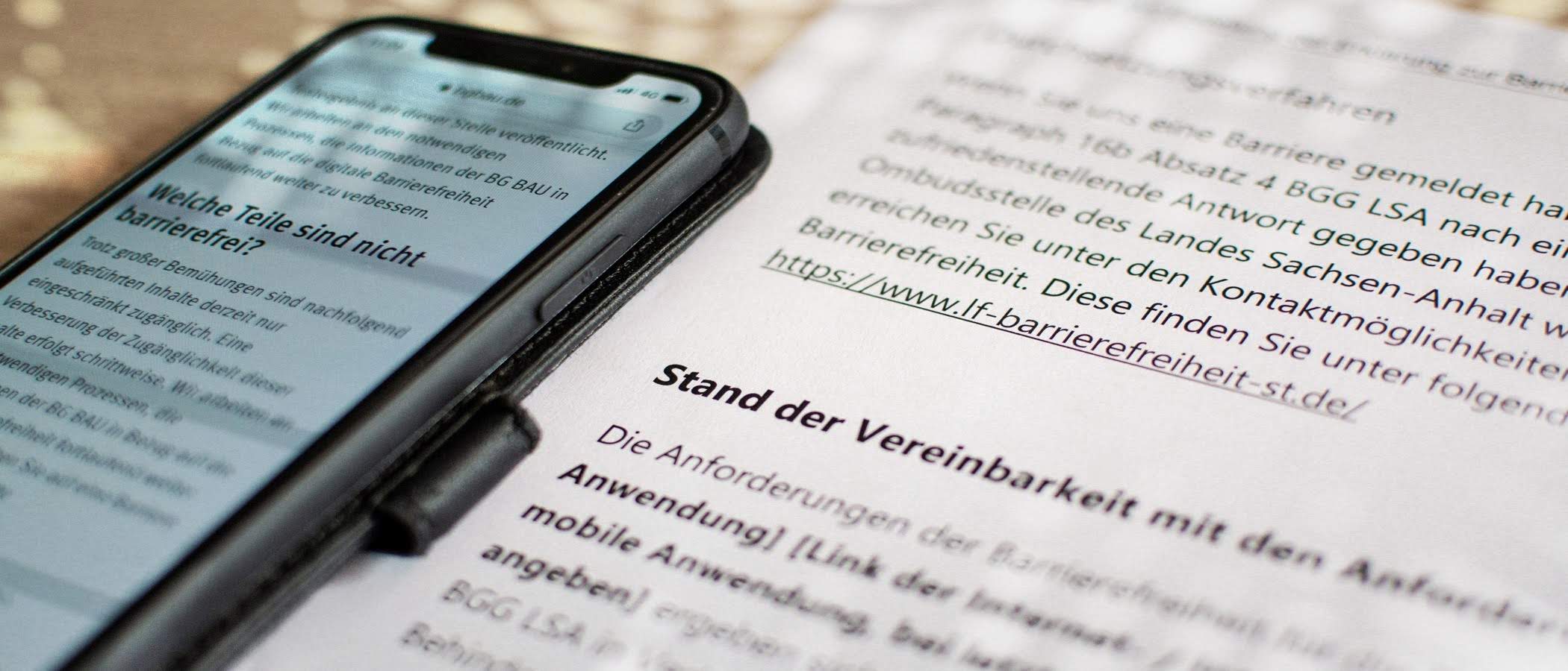 auf einem Schreibtisch liegt eine ausgedruckte Erklärung zur Barrierefreiheit und ein Smartphone, welches diese ebenfalls anzeigt - zur Artikelseite Erstellungshilfe für die Erklärung zur Barrierefreiheit